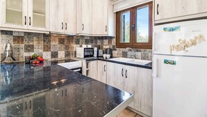 A kitchen with light wood cabinets, a black marble countertop, a white refrigerator, and a window with a view of greenery. - Villa Petra - Two Bedroom Villa, Sleeps 4 (Pilos Nestor)