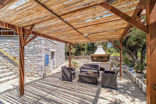A covered outdoor patio with stone walls, wicker furniture, and a barbecue area.