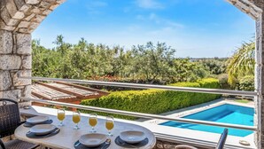 A stone archway leading to a dining area with a view of a swimming pool and lush greenery. - Villa Petra - Two Bedroom Villa, Sleeps 4 (Pilos Nestor)