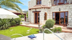 A two-story stone house with a patio, outdoor seating, and a well-maintained garden.