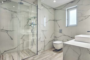 Ein modernes Badezimmer mit Marmorwänden, einer gläsernen Duschkabine, einer weißen Toilette und einem weißen Waschbecken.