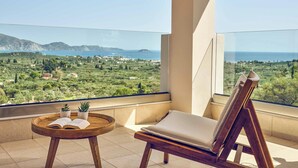 Un balcone con vista sul paesaggio costiero, una sedia di legno, un tavolino con un libro e due piante in vaso.