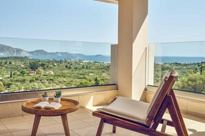 Ein Balkon mit Blick auf eine Küstenlandschaft, ein Holzstuhl, ein kleiner Tisch mit einem Buch und zwei Blumentöpfen.