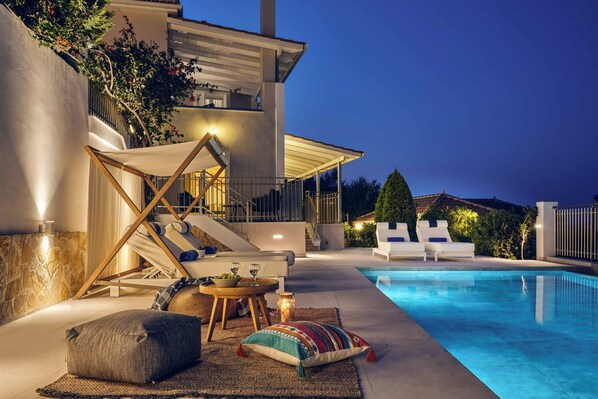 Un espace piscine extérieur moderne, doté de chaises longues, d’un ensemble de mobilier de jardin et d’un escalier menant à un balcon.