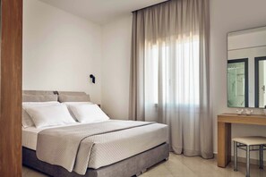 Ein Schlafzimmer mit einem Bett, einem Nachttisch, einem Sessel, einem großen Fenster mit Vorhängen und einem Spiegel über dem Tisch.