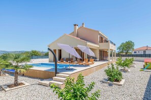 Une maison moderne à deux étages, dotée d’une piscine, d’un espace de détente extérieur et offrant une vue sur la mer.
