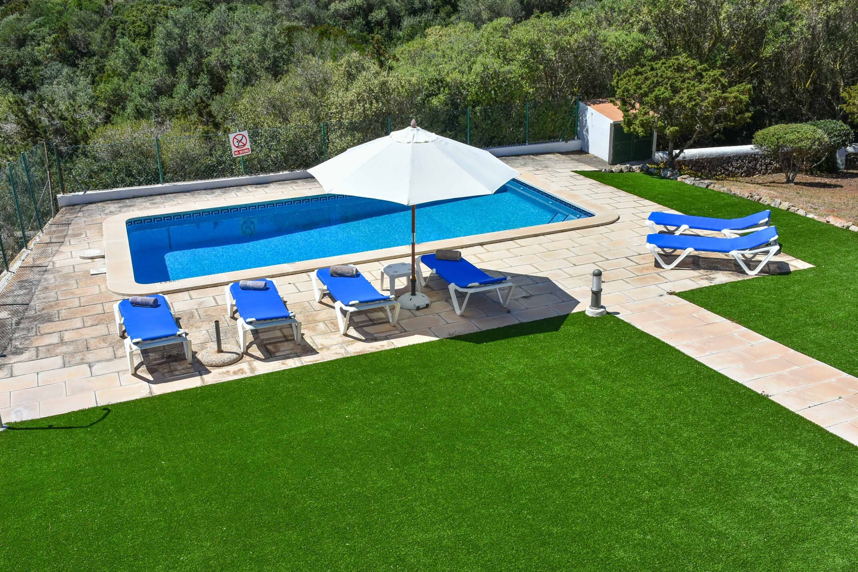 Ein rechteckiger Swimmingpool mit einem weißen Sonnenschirm, umgeben von blauen Liegestühlen und einer kleinen weißen Struktur.
