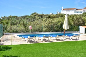 A swimming pool with lounge chairs and a no swimming sign, surrounded by a well-maintained lawn and a hill with trees. - Villa Marina - Three Bedroom Villa, Sleeps 6 (Ciutadella de Menorca)
