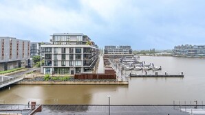 A modern waterfront building with multiple floors, a dock with boats, and a clear view of the water.