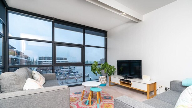 A modern living room with a large window, grey sofas, a TV, and a colorful rug.