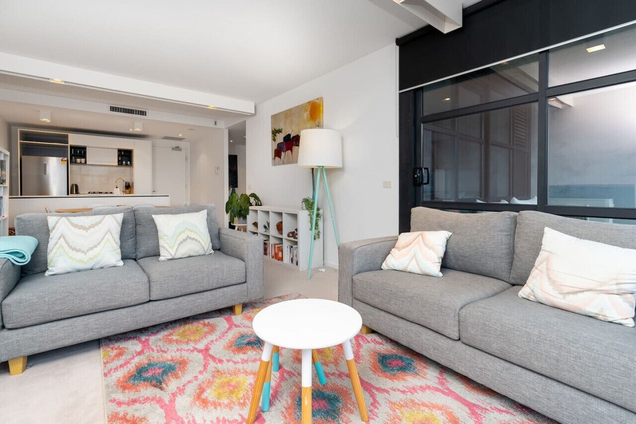 Ein modernes Wohnzimmer mit zwei grauen Sofas, einem weißen Couchtisch und einem farbenfrohen Teppich.
