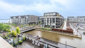 A riverside view of a modern building with a bridge, outdoor seating, and a waterfront promenade.