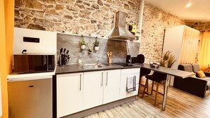 A kitchen with a stone wall, a microwave, a sink, and a bar area with stools. - Le Cocon Charmant Studio (Nîmes)