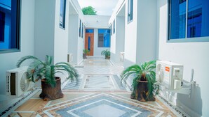 Un pasillo moderno con piso de diseño geométrico, plantas en macetas y una puerta central que da a otra habitación.