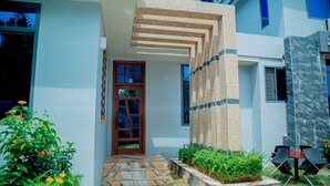 Un edificio moderno con una escalera de piedra que conduce a una puerta, rodeado de follaje y un pequeño espacio de estar al aire libre.