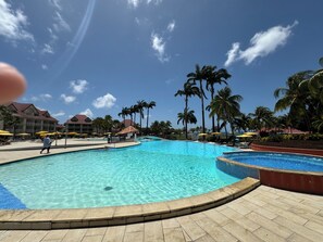 Una piscina grande con agua cristalina, rodeada de palmeras y un edificio de hotel con varios balcones.