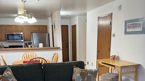 A living room with a sofa, a wooden coffee table, and a kitchen in the background. -  1 bdrm condo. Indoor parking garage. Secure bldg access.  90 day minimum stay (Anchorage)