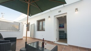 Un patio con mobiliario de mimbre, una mesa de vidrio y una botella de vino.