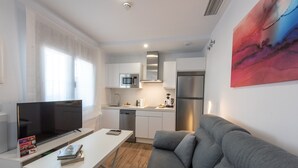 Una cocina moderna con microondas integrado, electrodomésticos de acero inoxidable y un comedor con mesa blanca y sofá gris.