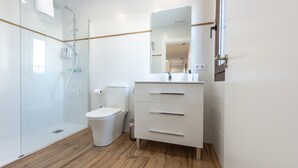 Un baño moderno con cabina de ducha de vidrio, un inodoro y un tocador con espejo.