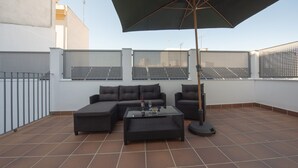 Una terraza en la azotea con un sofá modular, una mesita de centro y una sombrilla.
