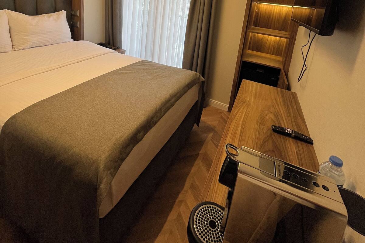 Habitación de hotel con cama, escritorio con computadora portátil, televisor montado en la pared y ventana con cortinas.