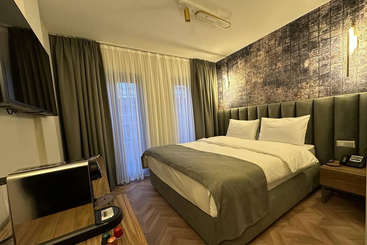 Habitación de hotel con una cama grande, un escritorio con una computadora portátil, un televisor y una pared con textura.