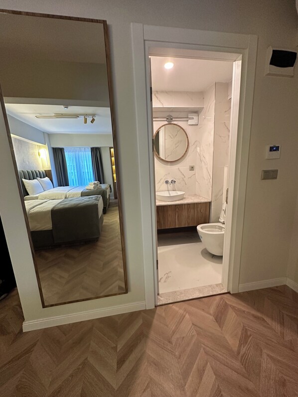 A hotel room with a bed, a bathroom with a sink and toilet, and a mirror reflecting the room. - Iris Han Hotel (Istanbul)