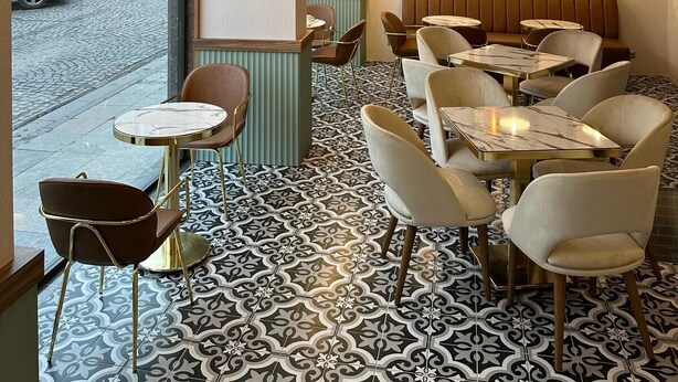 A restaurant interior with patterned flooring, multiple seating arrangements, hanging pendant lights, and large windows with a view of the street. - Iris Han Hotel (Istanbul)