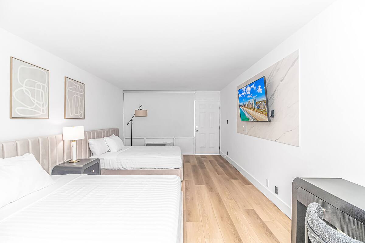 A hotel room with two beds, a TV on the wall, and artwork on the walls.