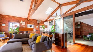 A modern living room with exposed wooden beams, a brick wall, and a large window.