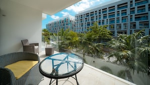 A balcony with wicker furniture, a glass table, and a view of a modern building with multiple floors and balconies. - Yucatán - 1 Bedroom in Playa Near 5th At 38th Street (Playa del Carmen)