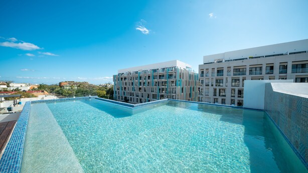 A clear blue swimming pool with a tiled edge, surrounded by modern buildings with balconies and large windows. - Yucatán - 1 Bedroom in Playa Near 5th At 38th Street (Playa del Carmen)