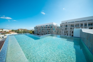 A clear blue swimming pool with a tiled edge, surrounded by modern buildings with balconies and large windows. - Yucatán - 1 Bedroom in Playa Near 5th At 38th Street (Playa del Carmen)