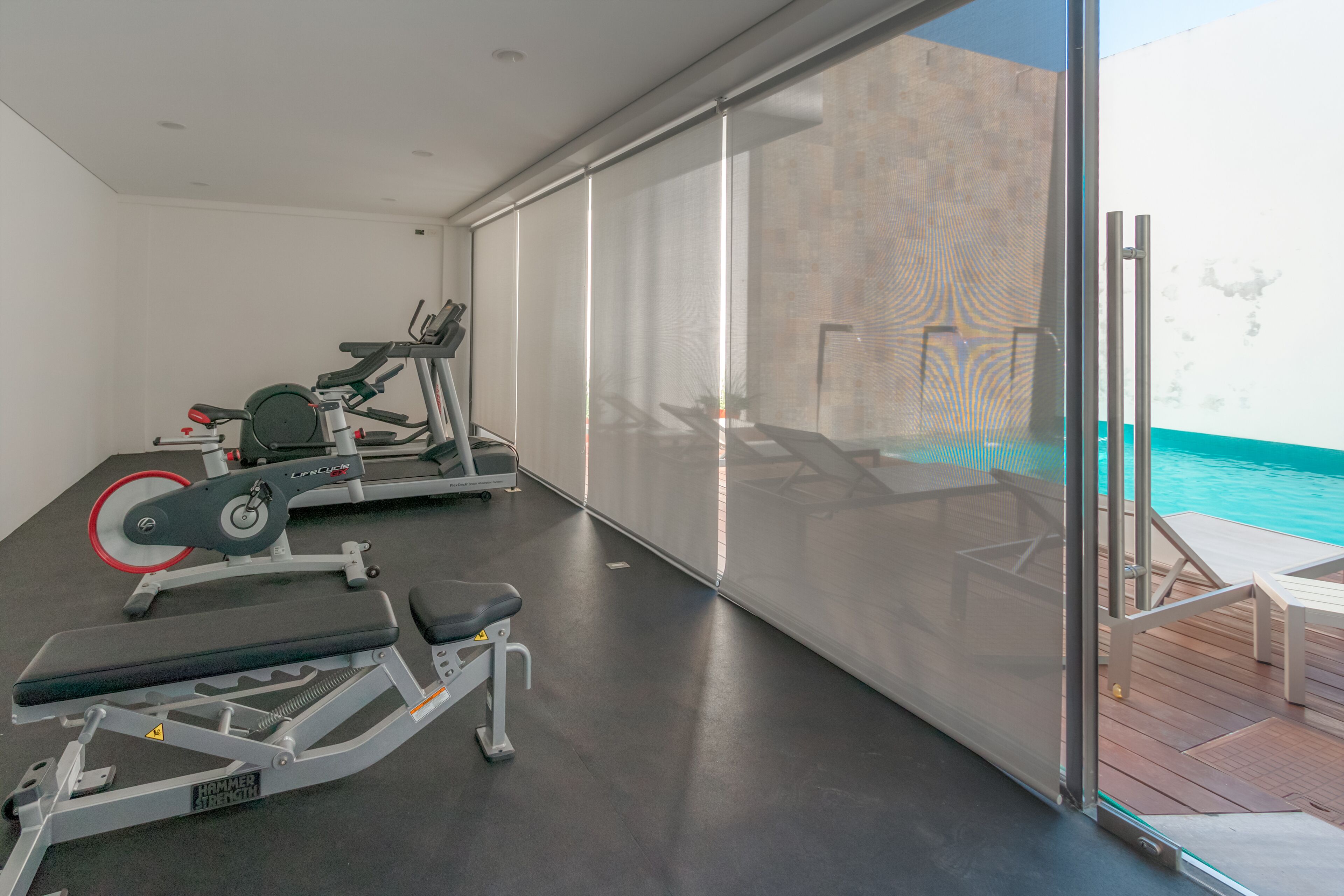 Gimnasio con equipo de ejercicio, una banca y vistas a una piscina.