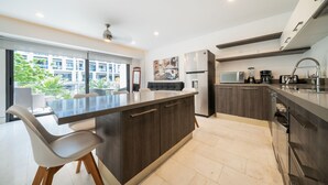 A modern kitchen with a central island, dark cabinetry, and a view of a residential building. - Yucatán - 1 Bedroom in Playa Near 5th At 38th Street (Playa del Carmen)