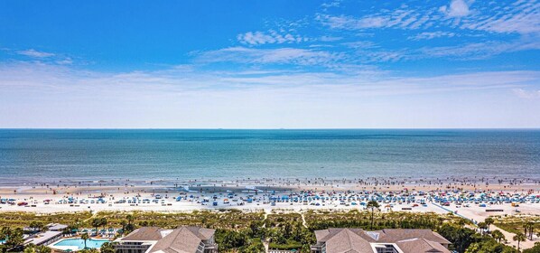 A beach with umbrellas and people, a pool, and houses in the foreground. - 321 Oceanfront Villa | Walk to Coligny + Pools | Washer/Dryer (Hilton Head Island)