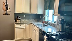 A kitchen with white cabinets, a black stove, and a window with curtains. - Entire Home N. Conway - Central Location, Saco, Skiing, Shopping (Conway)