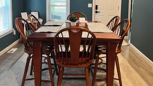 A dining room with a wooden table and chairs, a white door, and a window with blinds. - Entire Home N. Conway - Central Location, Saco, Skiing, Shopping (Conway)