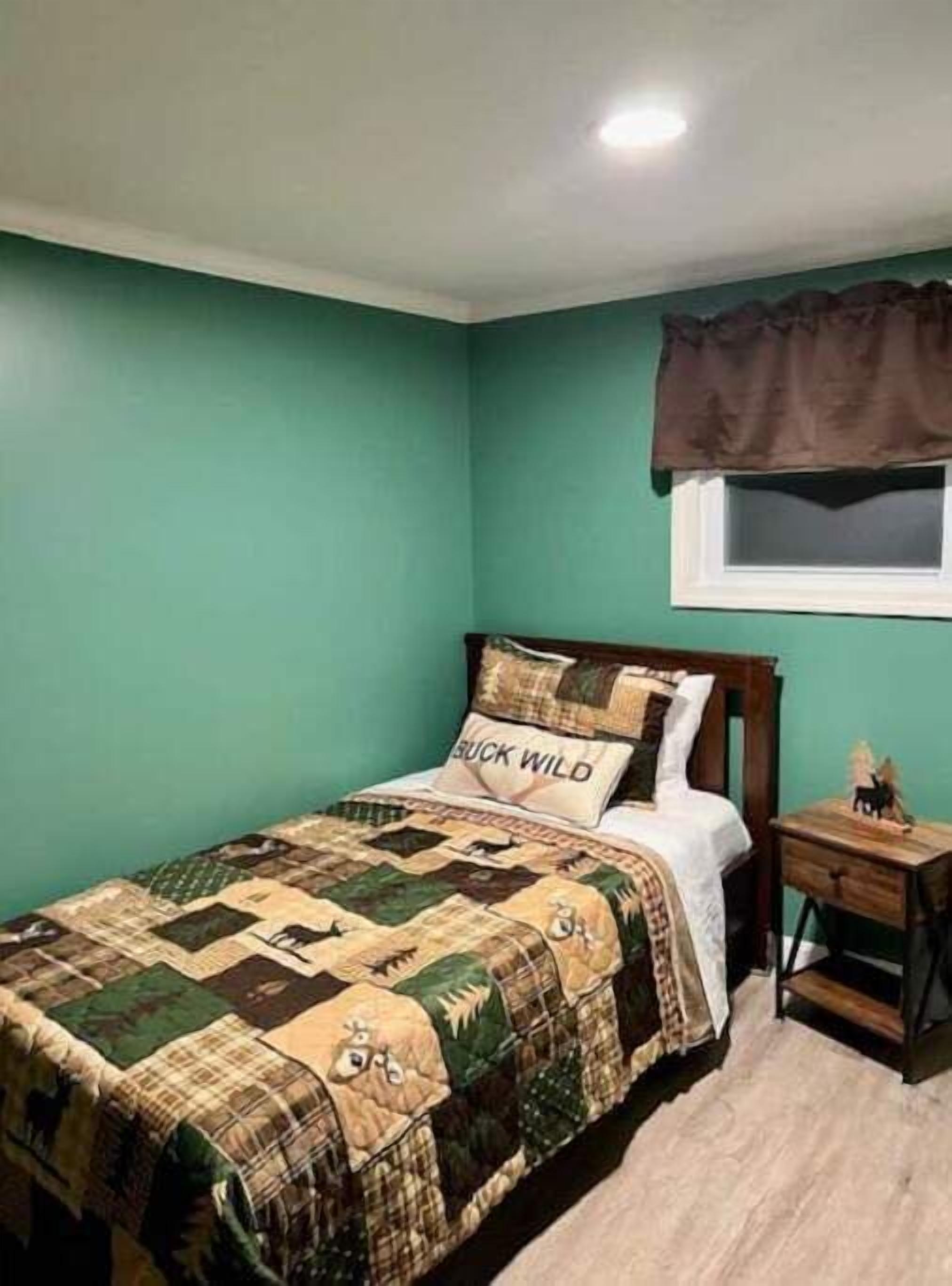 Une chambre à coucher comprenant un lit, une table de chevet, une fenêtre avec un lambrequin marron et un mur peint en vert.