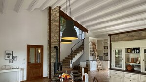 Un comedor amplio con una larga mesa de madera dispuesta para una comida, una pared de piedra y una escalera que sube a un nivel superior.