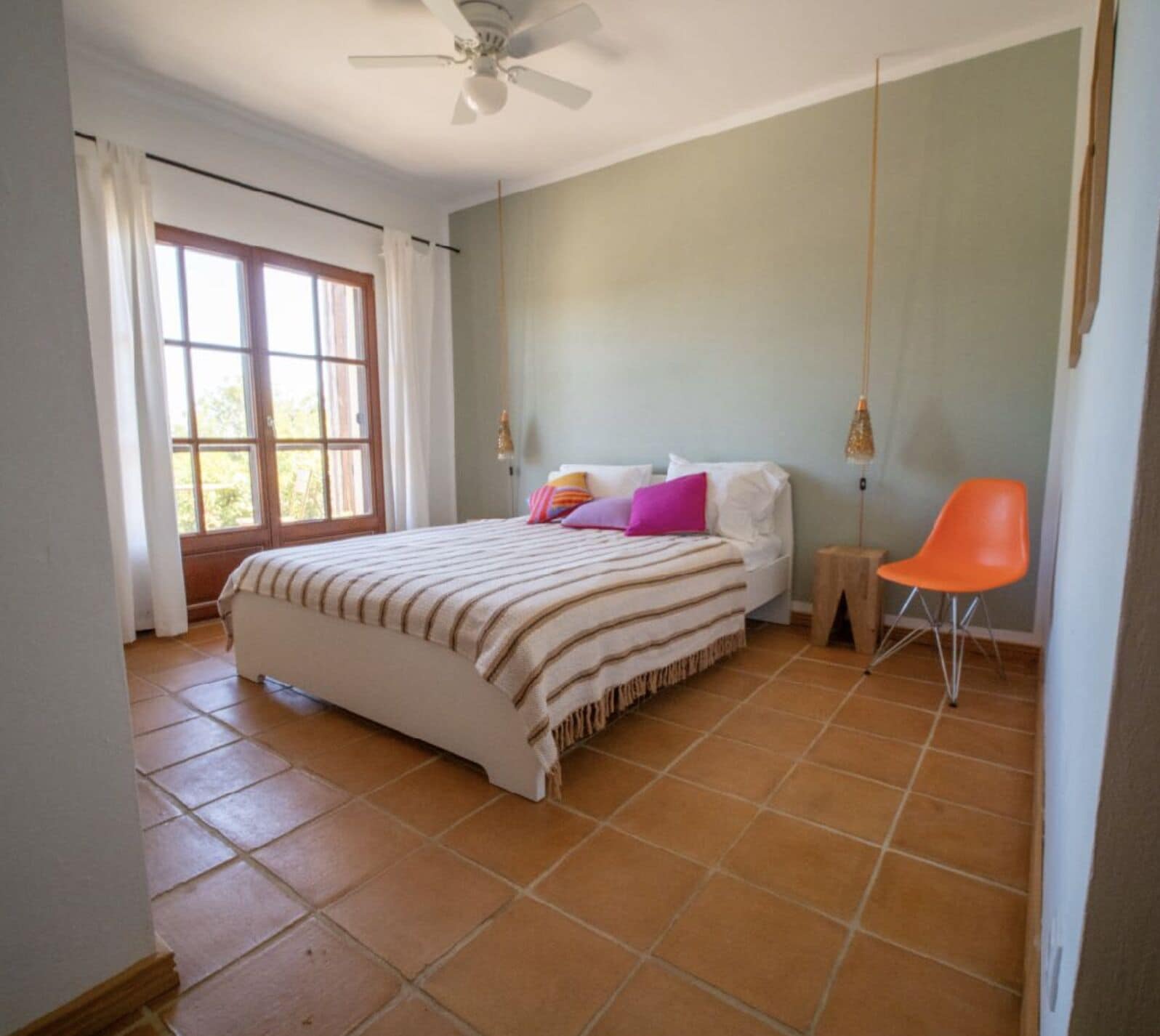 A bedroom with a bed, a window, a chair, and a ceiling fan.