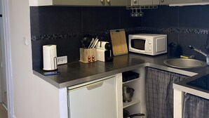 Eine kompakte Küche mit grauen Schränken, einer Mikrowelle, einem Spülbecken und einem kleinen Kühlschrank.