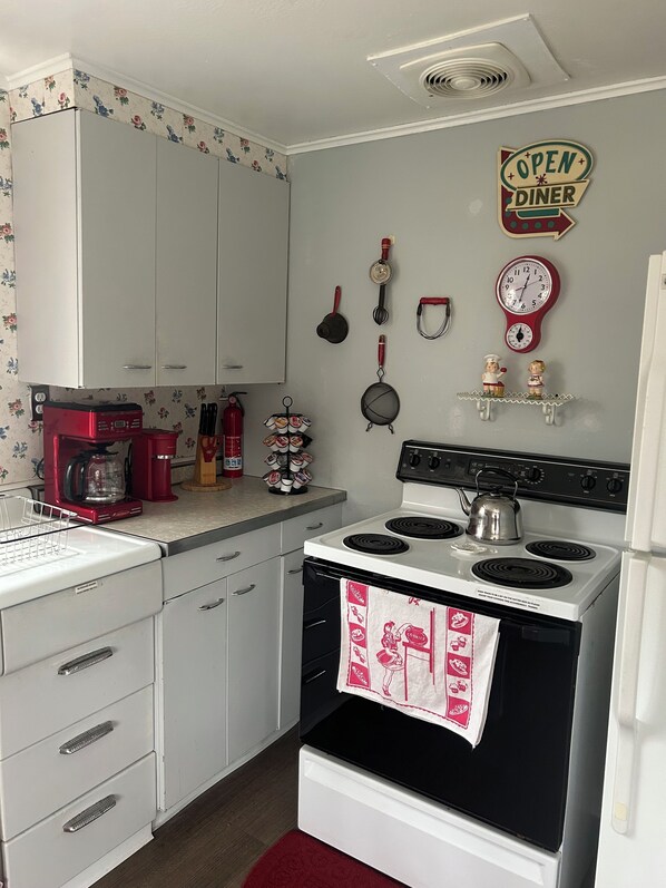 A kitchen with white cabinets, a red coffee maker, a stove, and a wall clock.