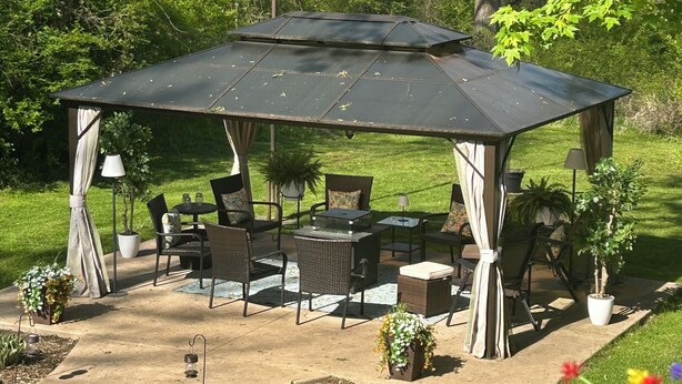Veranda esterna coperta con posti a sedere e tavoli, immersa nel verde e alberi.