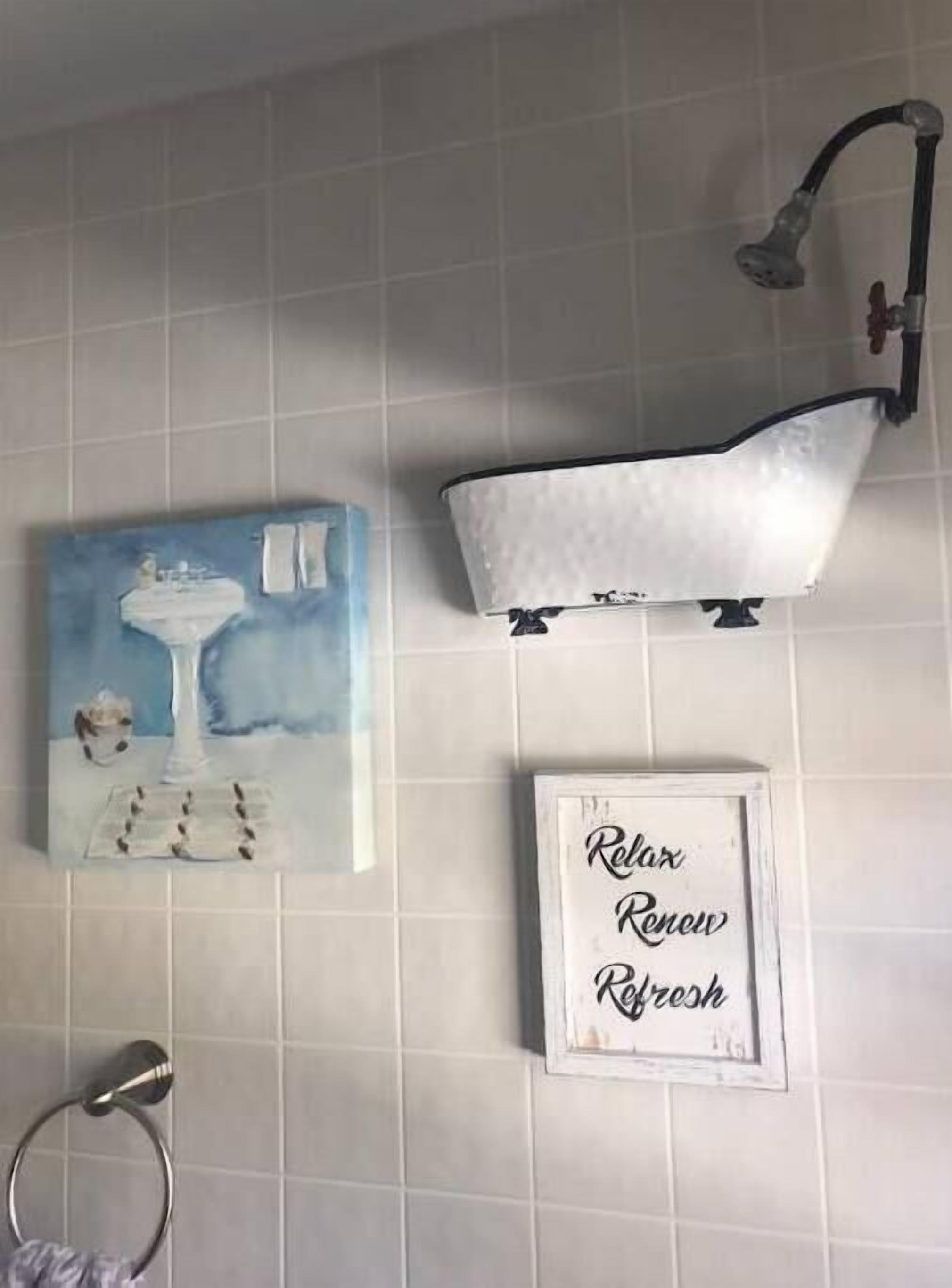 Um banheiro com uma banheira branca, uma placa emoldurada com a frase 'Relaxar Renovar Revigorar' e uma pintura de um vaso e flores na parede.