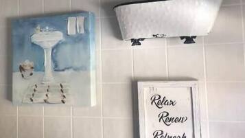 Um banheiro com uma banheira branca, uma placa emoldurada com a frase 'Relaxar Renovar Revigorar' e uma pintura de um vaso e flores na parede.