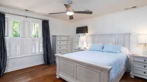 A bedroom with a large bed, a ceiling fan, a dresser, and a window with shutters.