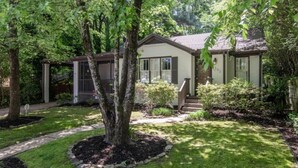 A two-story house with a front porch, a covered patio, and a well-maintained garden with a large tree in the center.