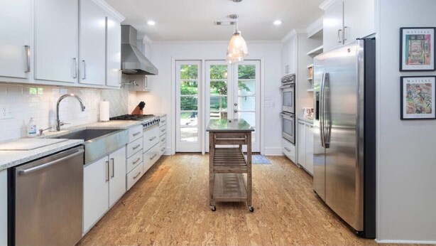 A modern kitchen with white cabinets, stainless steel appliances, and a wooden floor.